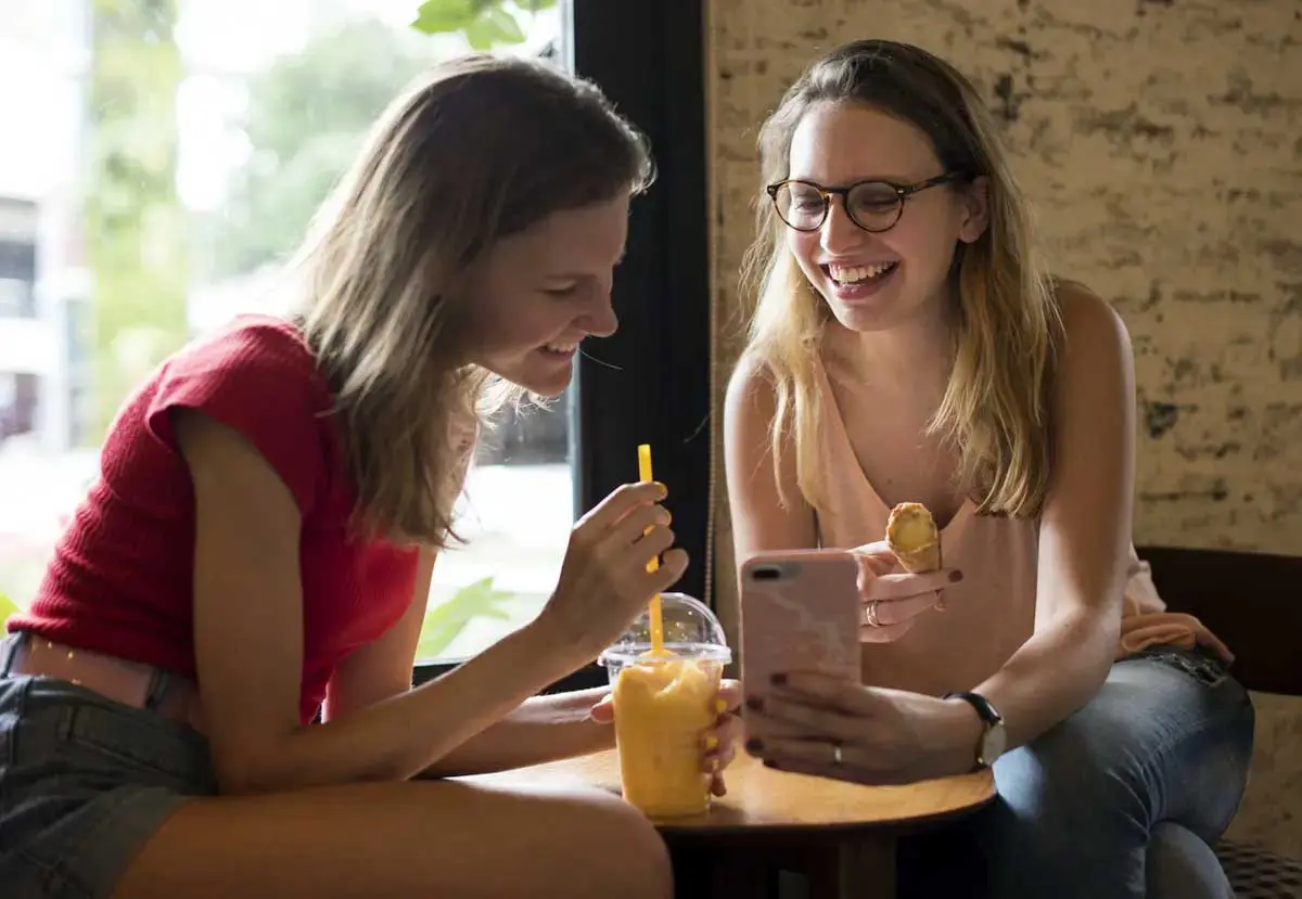 Two students look at phone while having a snack